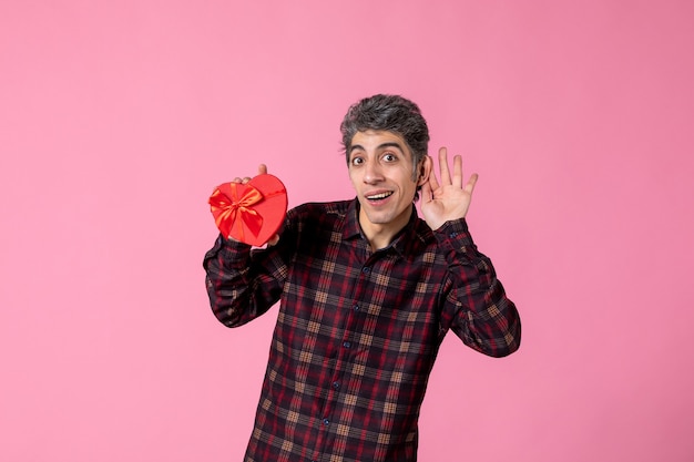 Vista frontal joven sosteniendo presente en forma de corazón rojo en la pared rosa