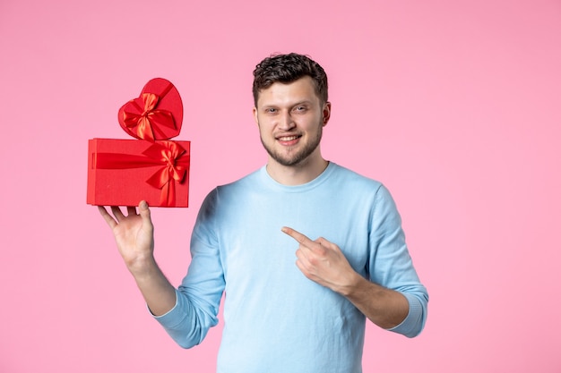 Vista frontal joven sosteniendo regalos en paquetes rojos sobre fondo rosa amor fecha matrimonio femenino sensual día de la mujer marzo igualdad diversión