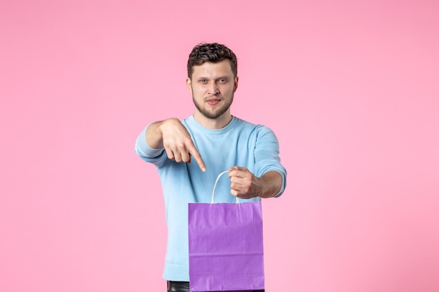 Vista frontal joven varón sosteniendo presente en paquete morado sobre fondo rosa parque de igualdad sensual día de la mujer marcha amor fecha femenina diversión