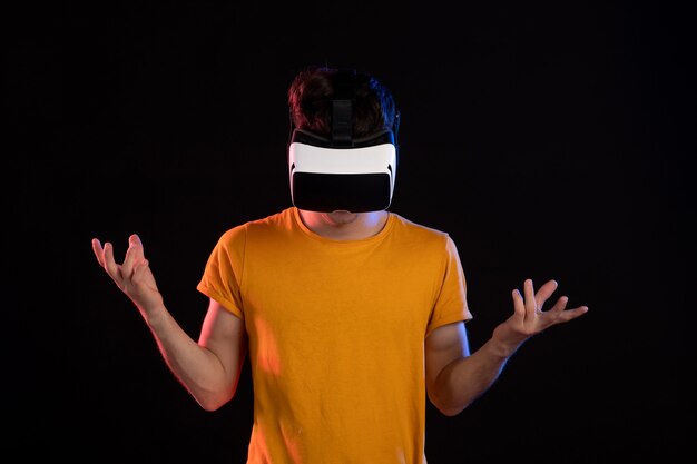 Vista frontal del joven vestido con casco de realidad virtual en la pared oscura