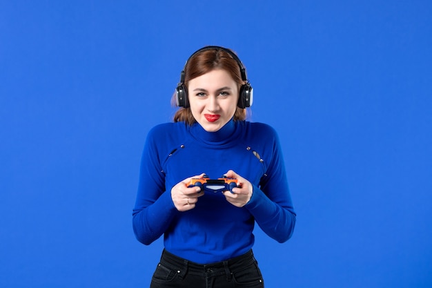 Vista frontal jugador femenino con auriculares y gamepad sobre fondo azul video sofá niña adulta joven jugador ganador juvenil virtual