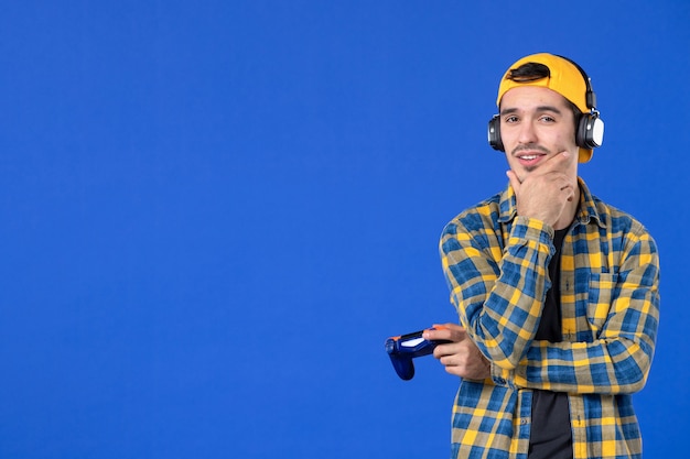 Vista frontal jugador masculino con gamepad jugando videojuegos sobre fondo azul video virtual fútbol jugador adolescente ganando alegría joven adulto