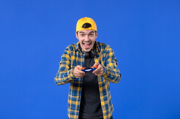 Foto vista frontal del jugador masculino con gamepad naranja en la pared azul