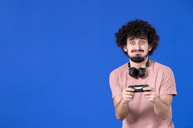 Vista frontal jugador masculino jugando videojuegos con gamepad sobre fondo azul ganador adolescente adulto alegría joven sofá virtual jugador juvenil