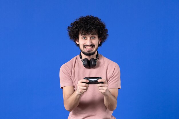 Vista frontal jugador masculino jugando videojuegos con gamepad sobre fondo azul joven virtual adolescente jugadores ganadores video juvenil fútbol adulto alegría