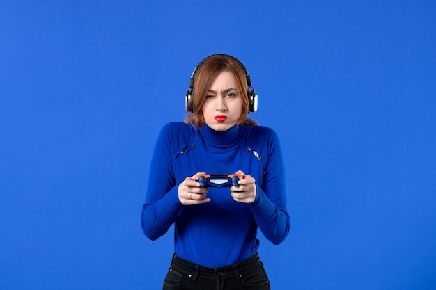 Vista frontal de la jugadora con auriculares y gamepad jugando videojuegos sobre fondo azul niña joven sofá alegría reproductor de video para adultos