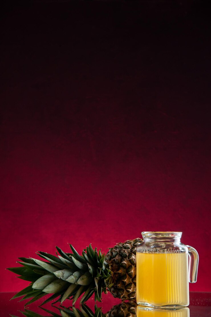 Vista frontal de jugo de piña en garrafa de piña que se establecen sobre fondo rojo oscuro