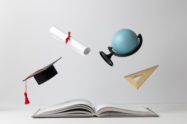 Vista frontal de un libro abierto, una gorra de graduación, un diploma, un globo terráqueo y un triángulo para el día de la educación