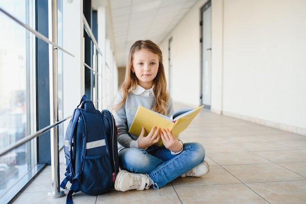 Vista frontal de una linda colegiala rubia sosteniendo muchas notas y libros coloridos Una adolescente inteligente sonriendo a la cámara de pie en el pasillo de la escuela internacional