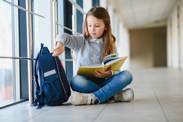 Vista frontal de una linda colegiala rubia sosteniendo muchas notas y libros coloridos Una adolescente inteligente sonriendo a la cámara de pie en el pasillo de la escuela internacional