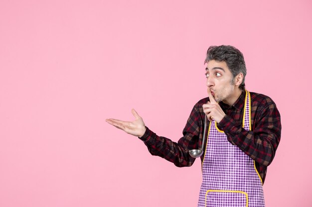 Vista frontal macho joven en el cabo sosteniendo una cuchara de sopa e interactuando con alguien sobre fondo rosa cocinar comida de cocina horizontal profesión marido trabajador