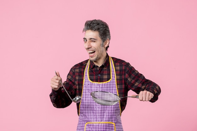 Vista frontal macho joven en capa con colador y cuchara sobre fondo rosa trabajador uniforme de alimentos marido cocina horizontal cocina sopa profesión cocinero