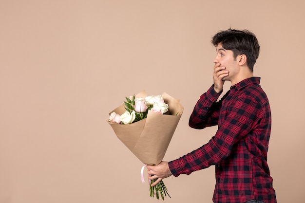 Vista frontal macho joven dando hermosas flores en la pared marrón