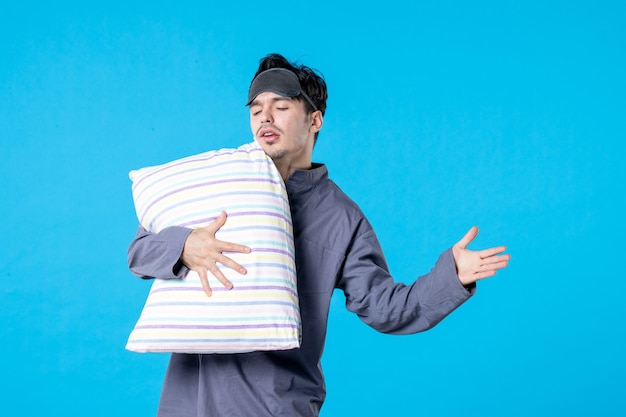 Vista frontal macho joven en pijama sosteniendo la almohada sobre fondo azul cama humana sueño sueño noche descanso pesadilla despertar tarde