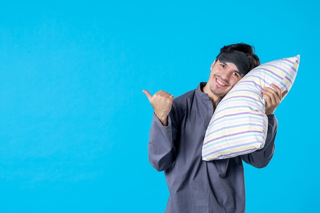 Vista frontal macho joven en pijama sosteniendo la almohada sobre fondo azul despertar reposo en cama color pesadilla sueño sueño humano noche