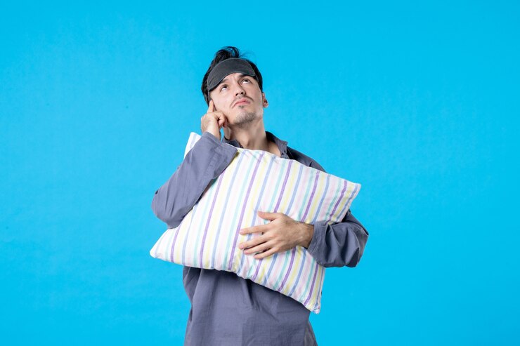 Vista frontal macho joven en pijama sosteniendo la almohada sobre fondo azul pesadilla de color cama humana descanso nocturno despertar tarde dormir sueños