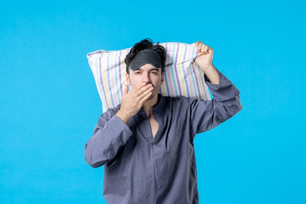 Vista frontal macho joven en pijama sosteniendo la almohada sobre fondo azul sueño dormir noche tarde cama humana pesadilla despertar color