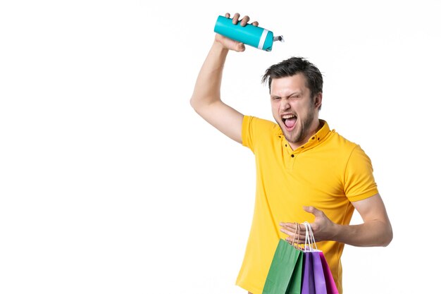 Foto vista frontal macho joven sosteniendo pequeños paquetes y termo sobre fondo blanco trabajo color deporte humano vendedor trabajador compras agua uniforme