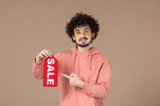 Vista frontal macho joven sosteniendo placa de venta sobre fondo marrón salón de piel terapia de compras spa facial cuidado de la piel masajeando colores
