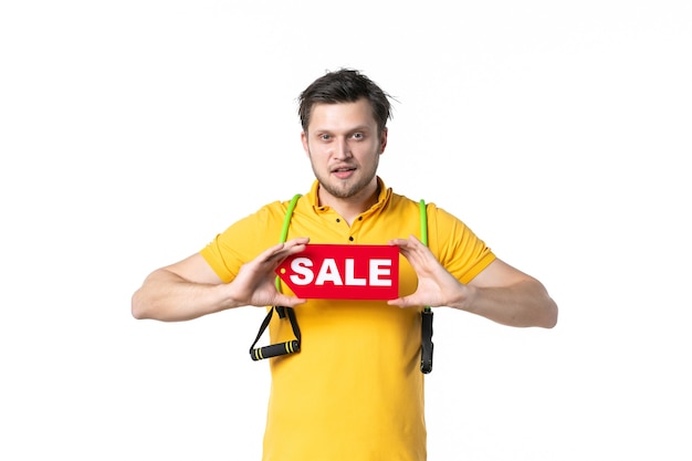 Vista frontal macho joven sosteniendo rojo venta placa de identificación escrita sobre fondo blanco trabajo deporte humano compras vendedor trabajador gimnasio uniforme dinero