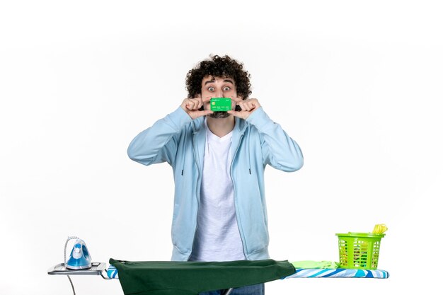 Foto vista frontal macho joven sosteniendo tarjeta bancaria verde sobre fondo blanco dinero lavandería quehaceres domésticos planchado humano emoción color limpio