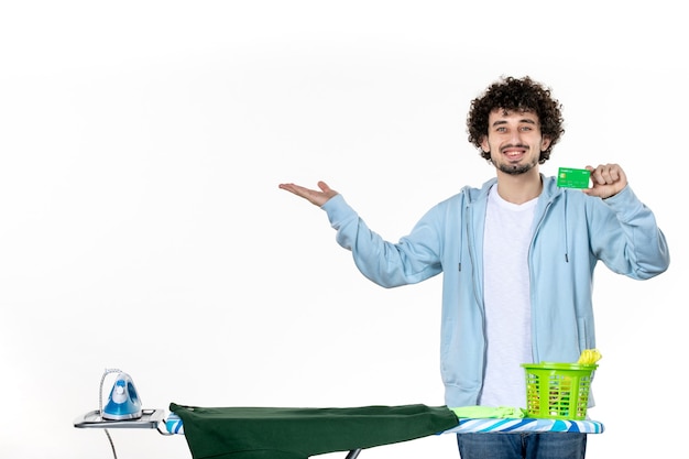 Vista frontal macho joven sosteniendo tarjeta bancaria verde sobre fondo blanco lavandería quehaceres domésticos limpieza humana dinero emoción planchado de color