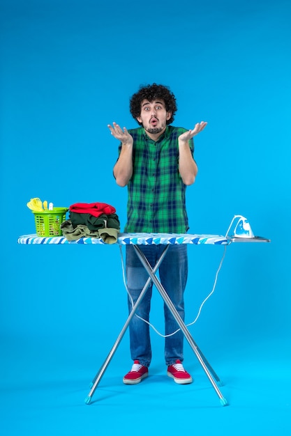 Vista frontal macho joven con tabla de planchar sobre fondo azul ropa de la casa lavadora limpia plancha humana