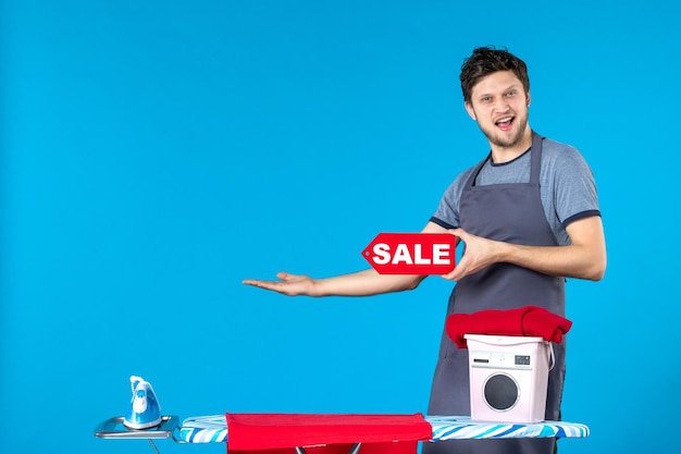 Vista frontal macho joven con venta rojo escrito en sus manos sobre fondo azul quehaceres domésticos lavandería compras lavadora limpieza