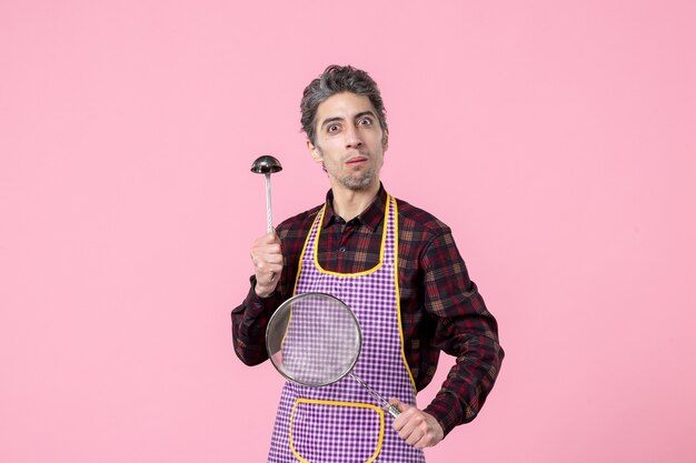 Vista frontal de los machos jóvenes en el cabo con un colador y una cuchara sobre fondo rosa comida cocina profesión uniforme trabajador cocinar cocina