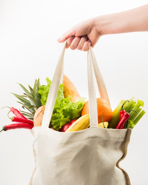 Vista frontal de la mano que sostiene la bolsa reutilizable con frutas y verduras