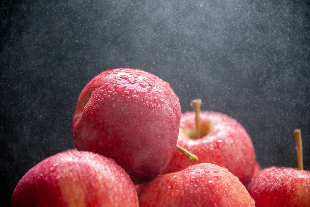 Vista frontal de manzanas rojas frescas apiladas en luz sobre fondo oscuro de onda