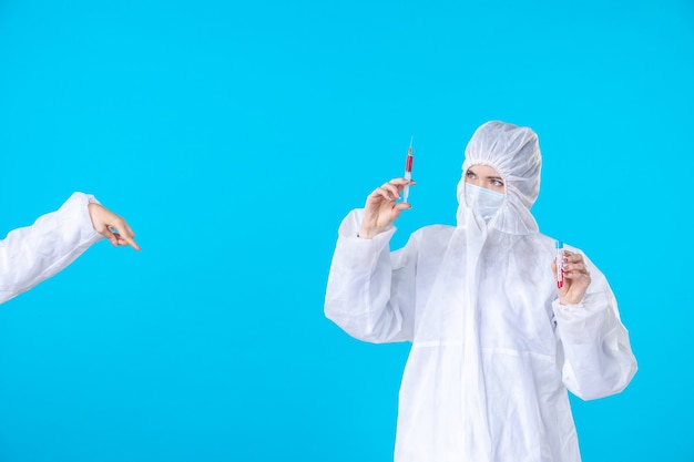 vista frontal médica em traje de proteção e máscara segurando injeção sobre fundo azul médico hospital covid pandemic vírus ciência