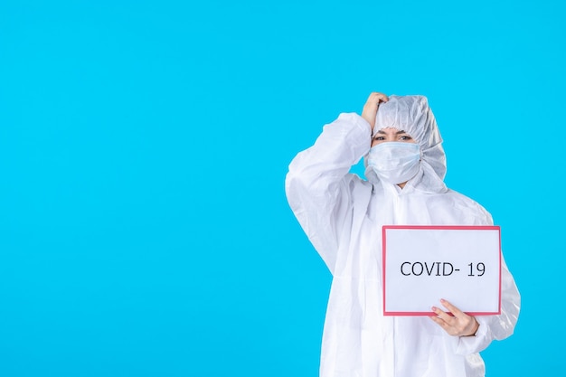 Foto vista frontal médica em traje de proteção e máscara sobre a cor de fundo azul covid- ciência saúde vírus isolamento pandêmico médico