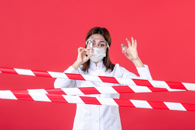 vista frontal médica segurando injeção e pequeno frasco na linha de saúde de fundo vermelho selado covid- vírus isolamento médico crime hospital