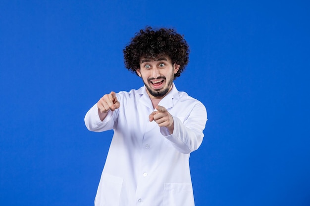 Vista frontal del médico masculino emocionado en traje médico sobre el virus de la vacuna de fondo azul covid- medicina pandémica medicina hospital coronavirus salud