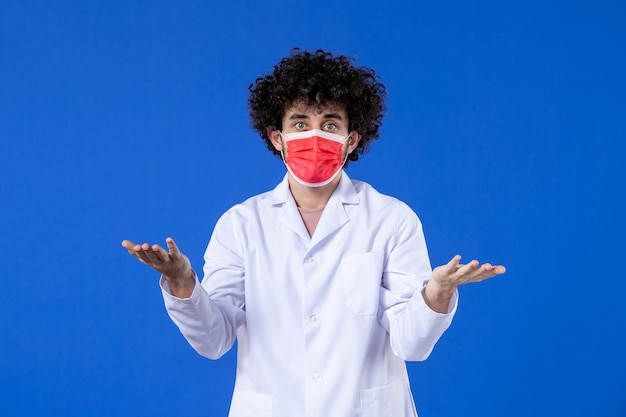 Vista frontal médico masculino en traje médico con máscara roja sobre fondo azul virus del hospital covid- fármaco de vacuna contra la pandemia de salud