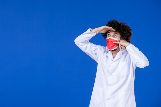 Vista frontal del médico masculino en traje médico y máscara sobre fondo azul vacuna salud medicamento hospital covid-coronavirus medicina virus