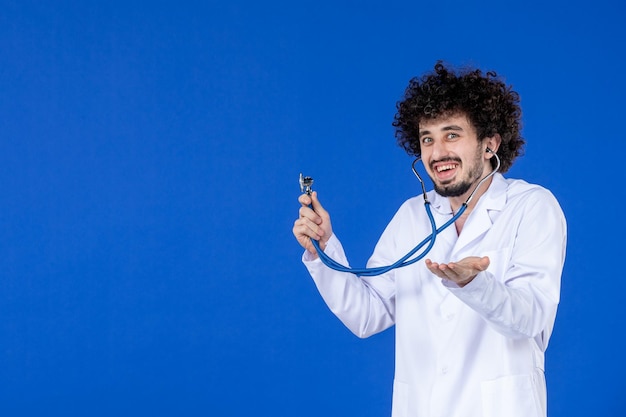 Vista frontal del médico de sexo masculino en traje médico con estetoscopio sobre superficie azul