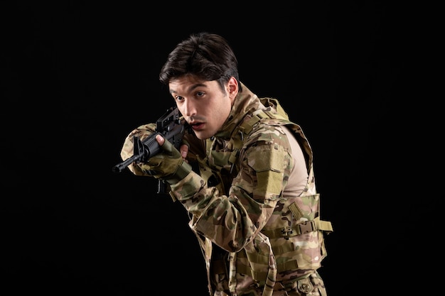 Vista frontal militar en uniforme apuntando con su rifle de tiro de estudio sobre una pared negra