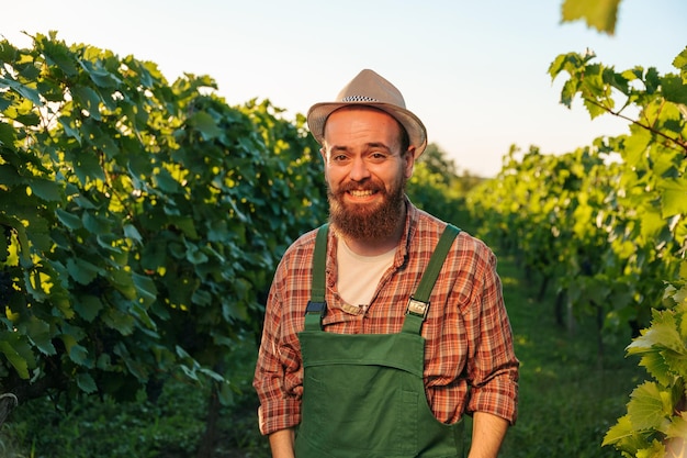 Vista frontal mirar cámara joven agricultor hombre enólogo viña trabajador risa sostener mano bolsillos resto