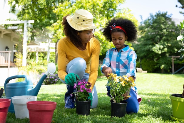 Vista frontal de una mujer afroamericana y su hija en el jardín, arrodilladas y macetas. Familia disfrutando del tiempo en casa, concepto de estilo de vida