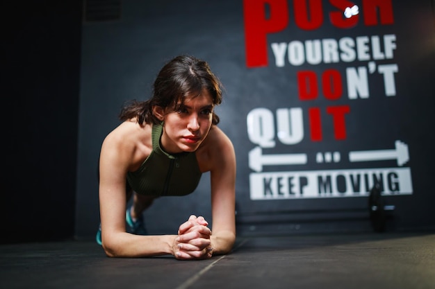 Vista frontal de una mujer bonita haciendo ejercicio en el gimnasio y posa en posición de tablón Es genial para los abdominales