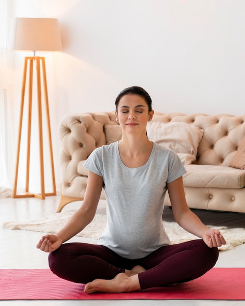 Vista frontal mujer embarazada meditando en interiores