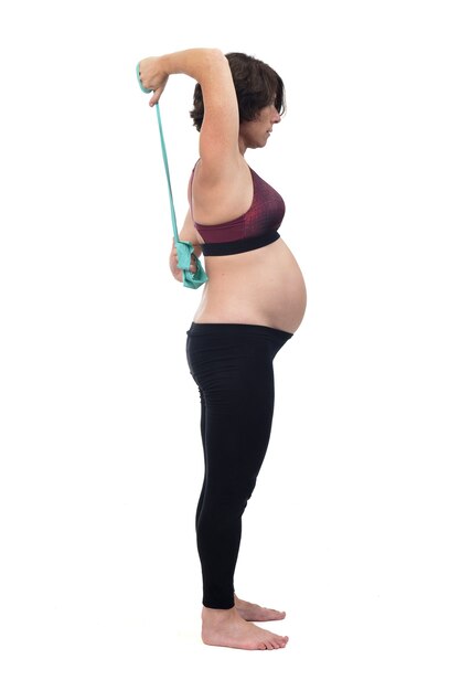 Vista frontal de una mujer embarazada de pie haciendo ejercicios de bandas de resistencia sobre fondo blanco.