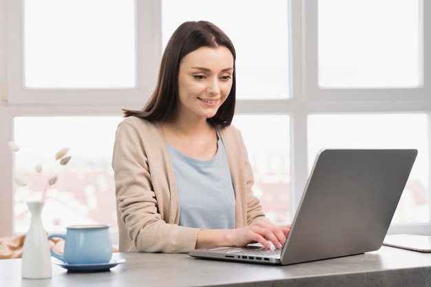 Vista frontal de la mujer en el escritorio trabajando desde casa en la computadora portátil