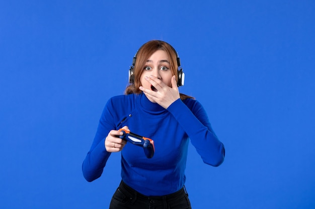 Vista frontal mujer gamer con auriculares y gamepad jugando videojuegos sobre fondo azul jugador niña joven sofá video ganador alegría virtual adulto joven