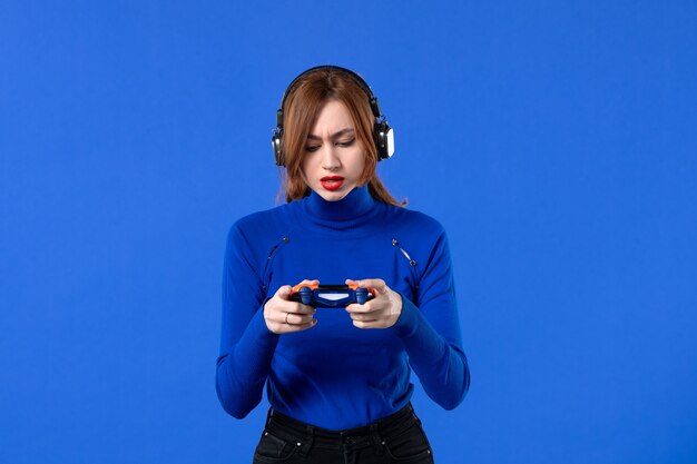 Vista frontal mujer gamer con auriculares y gamepad jugando videojuegos sobre fondo azul niña joven sofá ganando adultos reproductor de video alegría virtual