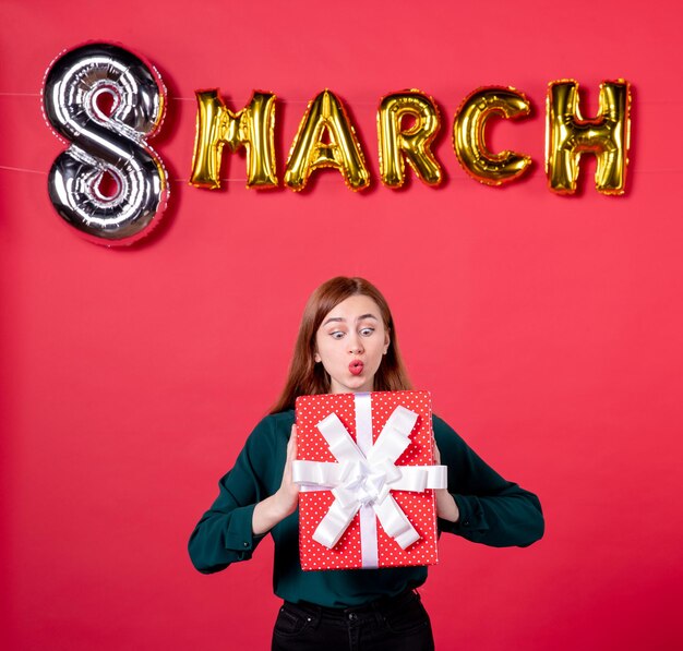 Vista frontal mujer joven con decoración de marzo y presente sobre fondo rojo regalo de amor femenino mujer sensual día de fiesta vogue