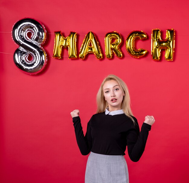 Vista frontal mujer joven con decoración de marzo sobre fondo rojo igualdad femenina vacaciones día de la mujer lujoso salón de pasión amor sensual