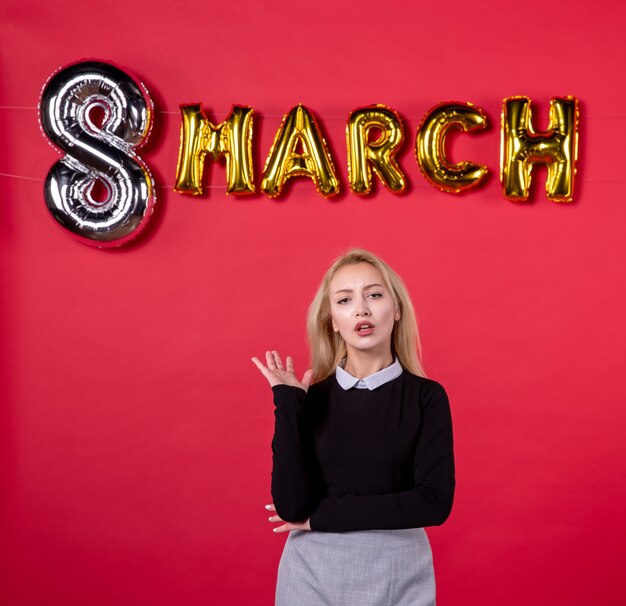 Vista frontal mujer joven con decoración de marzo sobre fondo rojo igualdad vacaciones día de la mujer amor sensual lujoso salón femenino